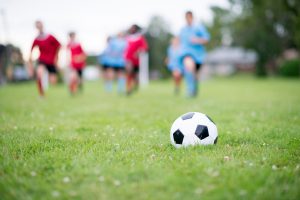 A multi-ethnic group of elementary age children are running up the field during the soccer game and are going to kick the soccer ball.